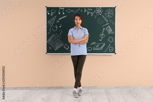 Female Asian PE teacher with soccer ball near blackboard in classroom