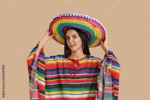 Beautiful young woman in Mexican sombrero hat on beige background