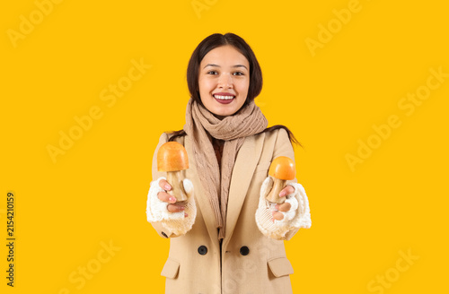 Beautiful young Asian woman in warm scarf decorative mushrooms on yellow back...