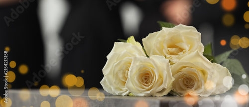 Foto White roses on a table with Blurred people in black suits and golden bokeh light