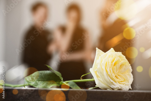Canvas Print White rose on a table with blurred people in the background, remembrance, loss,