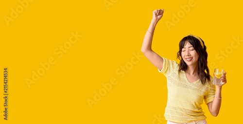 фотографія Happy young asian woman with a glass of refreshing lemon water raising her arm i