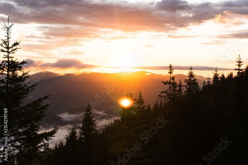 Sunrise mountain landscape with fog and sea of clouds, silhouettes of peaks glowing in warm sun rays
