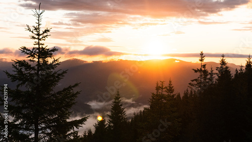 Sunrise mountain landscape with fog and sea of clouds, silhouettes of peaks glowing in warm sun rays