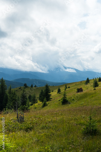 View of green mountain ridges covered with grass and silhouettes of peaks in soft sun rays
