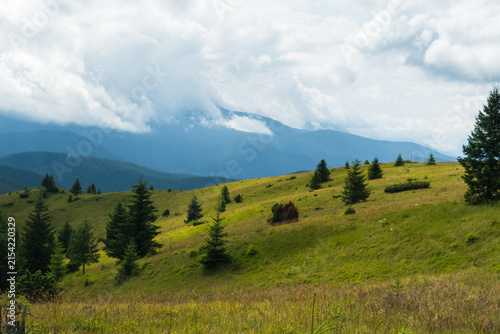 View of green mountain ridges covered with grass and silhouettes of peaks in soft sun rays
