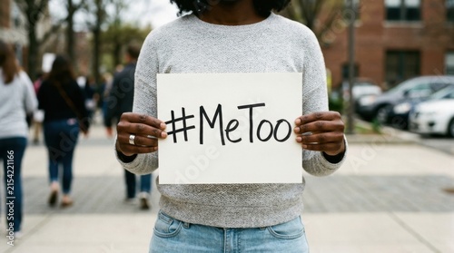 Empowered woman holds a white sign with the metoo hashtag while standing on a busy city sidewalk during a social justice protest, representing global movements against harassment and sexual