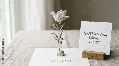 Minimalist white clay bird hanging over an olive branch with inspirational quotes on a rustic table surface, ideal for mental wellness, peaceful lifestyle, and home decor marketing materials. serenity