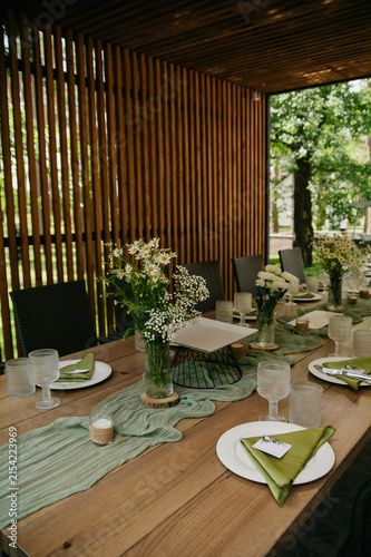 Interior of a banquet hall in the form of a gazebo in an open space with dishes, food, drinks and flowers in vases and napkins on the table for a wedding or anniversary celebration