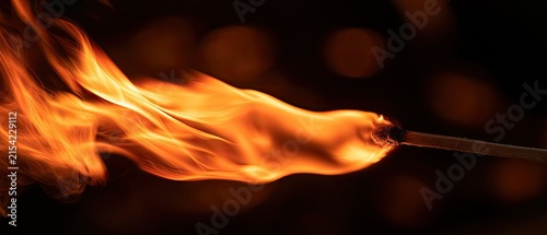 Close up of a burning matchstick with vibrant orange flames against a dark, blurred background