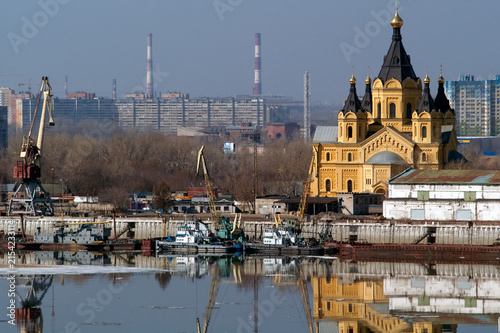 Bild auf Leinwand A yellow Orthodox cathedral on an industrial embankment with cranes, boats and a reflection of the cityscape in Nizhny Novgorod, Russia