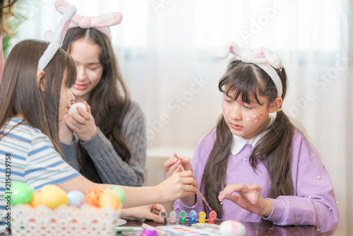 Konstfotografi A diverse family of four concentrating on painting a bright Easter egg by hand at a wooden coffee table strewn with brushes, paints and eggs on a happy holiday morning