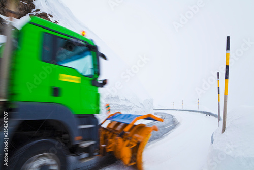 Green snowplow clears snow on a sinuous alpine road in Switzerland