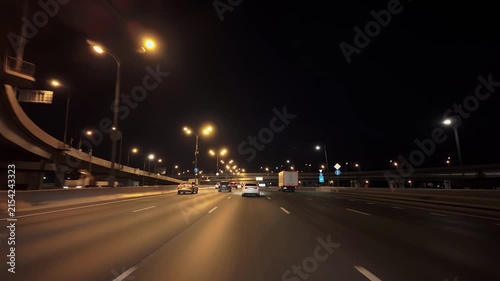 Evening commute under concrete overpasses with moving cars and warm streetlights