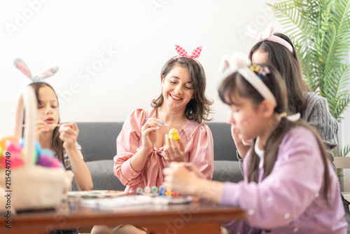 Photography A mother and two girls painting Easter eggs together with fine brushes at a wooden coffee table strewn with brushes, paints and eggs on a happy holiday morning