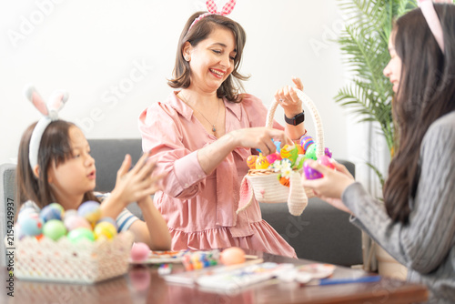 Принти на полотні A multiethnic family at home presenting a handful of colorful Easter eggs to the camera at a wooden coffee table strewn with brushes, paints and eggs on a happy holiday morning