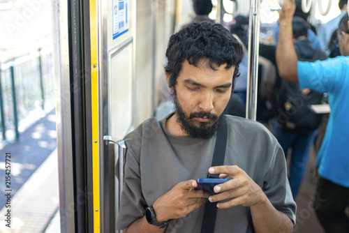 Male commuter using smartphone inside crowded public train