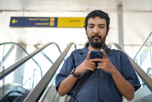 Male commuter using smartphone while riding escalator at transit station