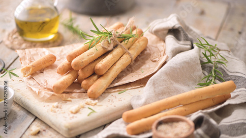 Crispy Italian breadsticks tied with fresh rosemary on a rustic wooden board