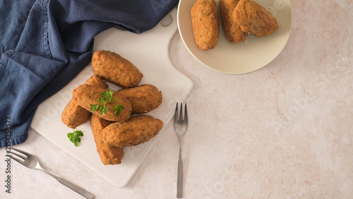 фотографія Golden fried croquettes with parsley on a white board and plate