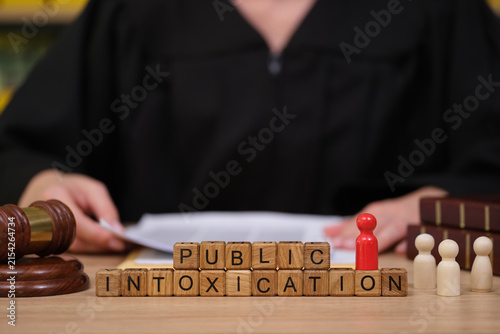 Foto In a courtroom, a judge in robes reviews documents while wooden blocks display the term public intoxication, highlighting legal consequences