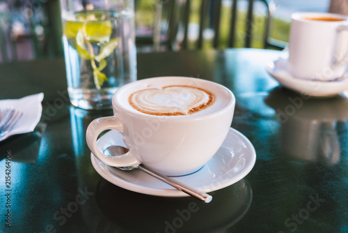 Cappuccino with latte art and spoon served on a white saucer in a cozy cafe
