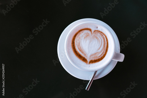 Cappuccino with latte art and spoon served on a white saucer in a cozy cafe