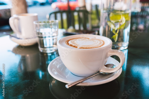 Cappuccino with latte art and spoon served on a white saucer in a cozy cafe