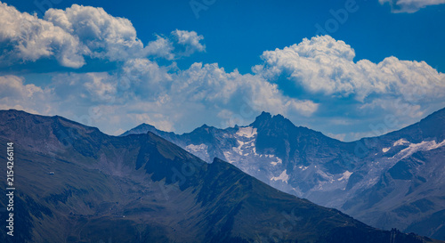 Fotografía Alpine mountain landscape featuring peaks and white clouds