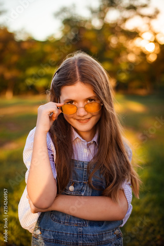 Obraz na płótnie playful young girl lowering yellow sunglasses with sly smile in park