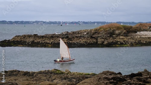 Coastal sailing boat navigates narrow waterway near rugged rocks