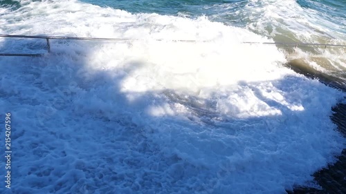 Waves crash against stone pier with metal railing