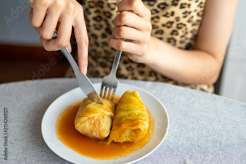 Person cuts a homemade cabbage roll with a fork and knife during a family meal. Shared food and homemade cooking illustrate comfort, everyday dining and the enjoyment of a family recipe