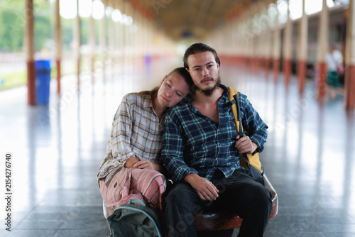 Bild auf Leinwand Young traveling couple resting on a train station bench, feeling exhausted durin