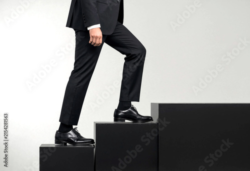 Businessman in formal black suit and polished shoes stepping up on black blocks symbolizing success and growth