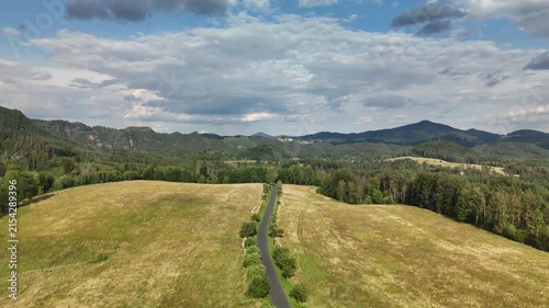 Empty country road crossing a dry golden meadow on a ridge above wooded hills
