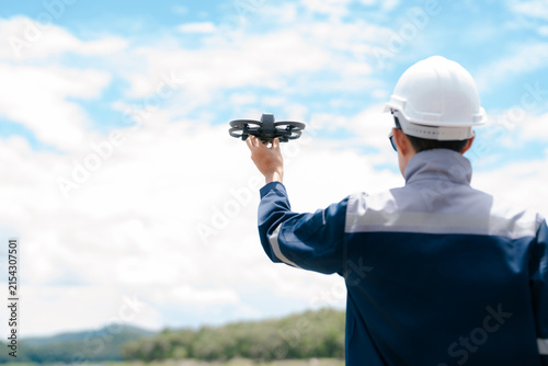 Asian engineer operates an industrial drone for aerial field survey, infrastructure inspection, environmental monitoring, and ecological assessment near a reservoir.