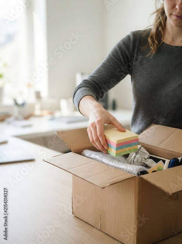 A woman carefully packing a cardboard box with stationery and office supplies