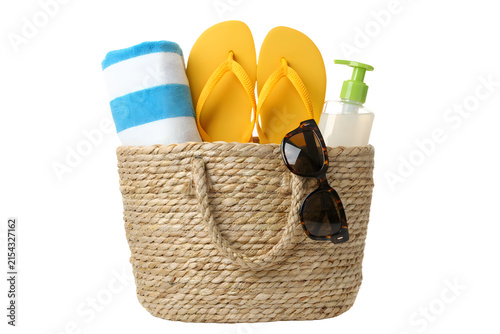 Summer beach essentials including yellow flip flops a rolled towel sunscreen and sunglasses in a woven basket on a black background