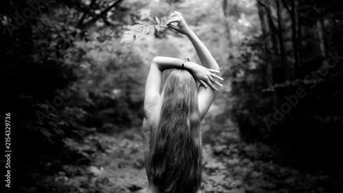 Woman with long hair standing in forest raising arm overhead.