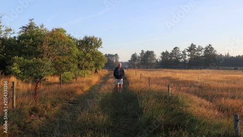 Hirtshals, Denmark A man walks in the early morning on a dirt road with lush fields. 