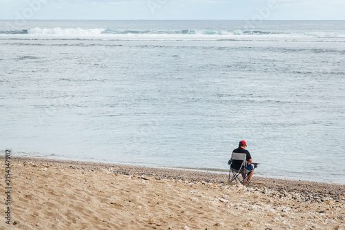 Une personne assise à la plage devant la mer regardant l'horizon.