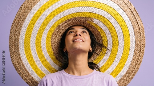 Smiling woman wearing large striped straw hat on purple background.
