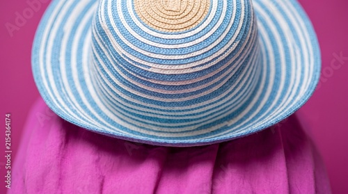 Striped summer sun hat on vibrant pink fabric background for vacation concept.