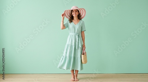 Stylish woman in mint green tiered dress and striped sun hat posing.