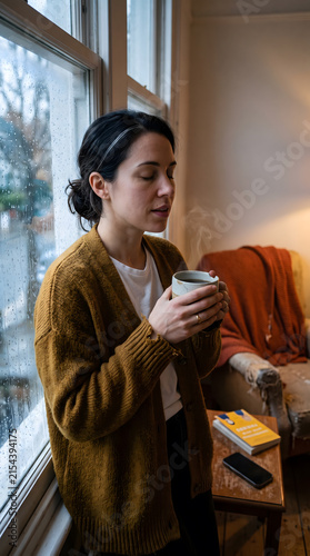 Woman in mustard cardigan exhaling tension by rain window with chipped ceramic mug, quiet digital detox