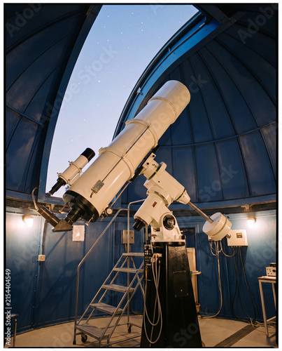 Large white research telescope on equatorial mount inside observatory dome with stars through open slit