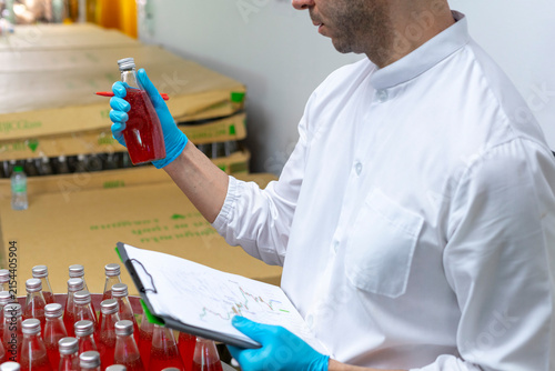 Portrait of mature male researcher with bottle of red beverage in bottle factory.