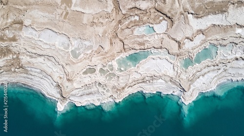 Dead Sea salt crystals edge vivid deep blue-green water in extraordinary white patterns in 19:6 ultra-wide nadir — Earth's lowest point as panoramic aerial art.