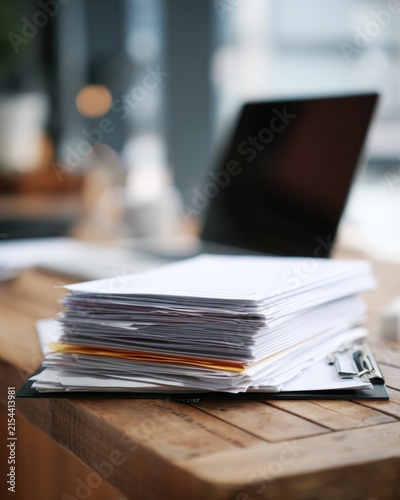 Stack of papers on clipboard on office desk with blurred laptop background